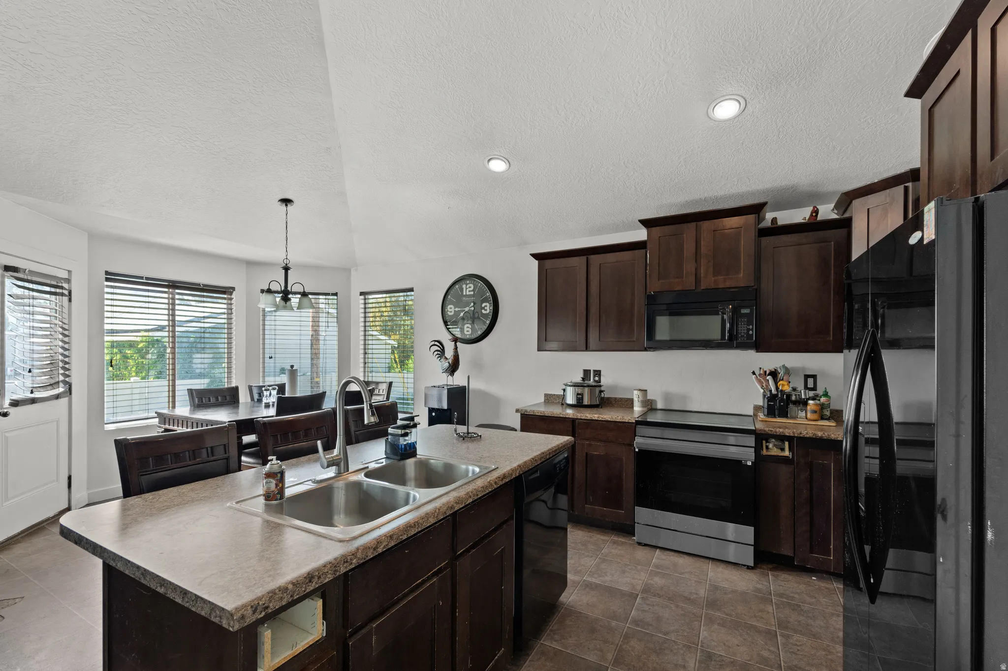 Kitchen featuring dark wood-finish cabinetry, stainless steel appliances, and a central island with a double basin sink