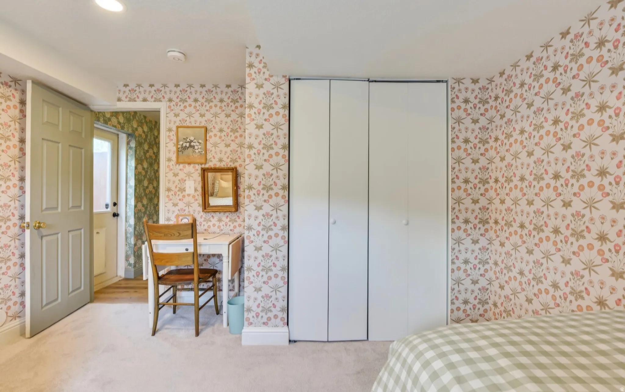 Carpeted room featuring a six-panel door, built-in bi-fold closet, and botanical pattern wallpaper