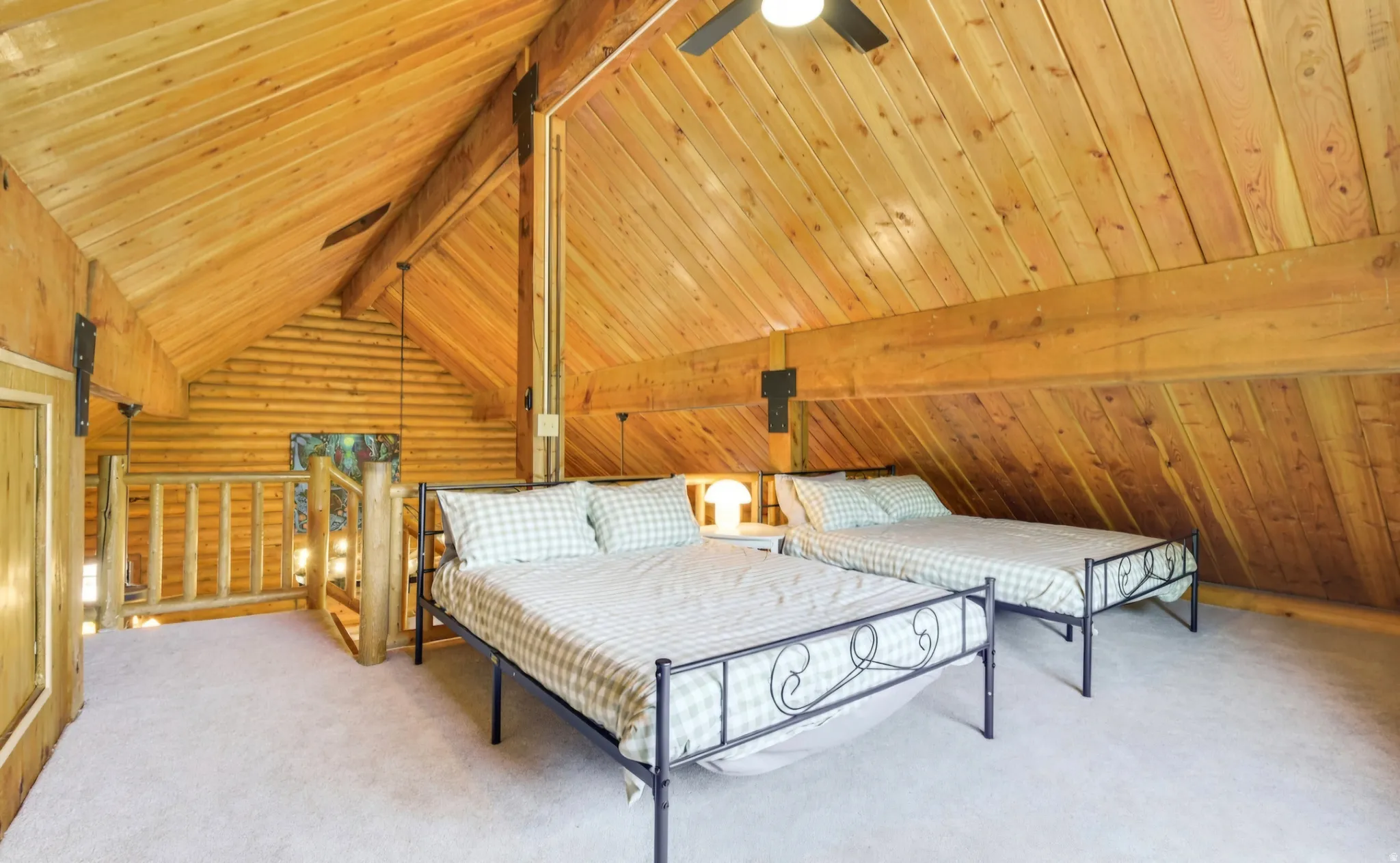 Vaulted wood-paneled ceiling with exposed beams, wood-plank walls, light-toned carpeting, and a rustic wood railing