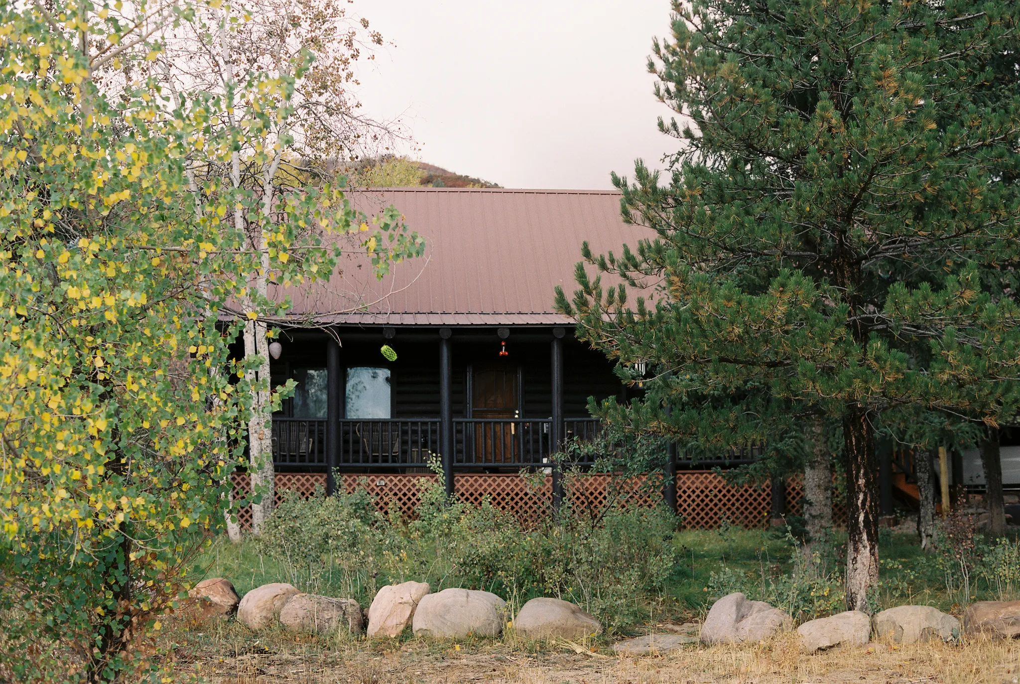Log cabin exterior featuring a covered porch, dark brown metal roof, and exposed natural wood siding