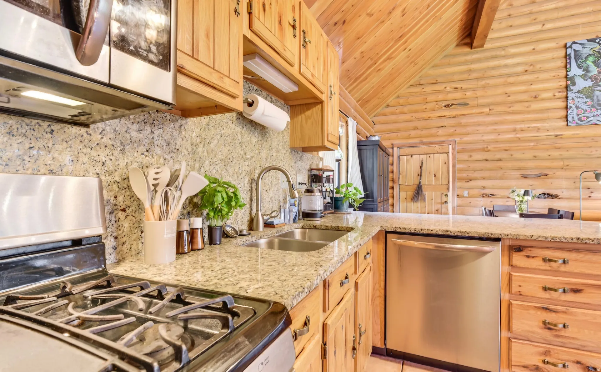 Kitchen featuring wood-finish cabinetry, granite-finish countertops, stainless steel appliances, a double basin sink, and a log cabin wall finish