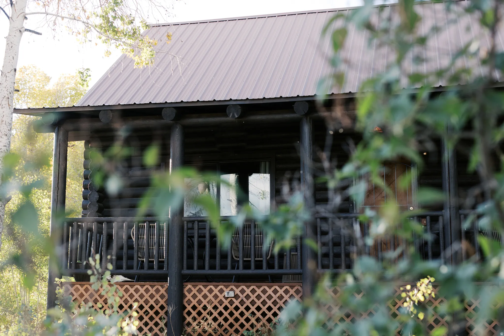Log cabin exterior featuring a covered porch with a railing, a metal roof, and lattice skirting