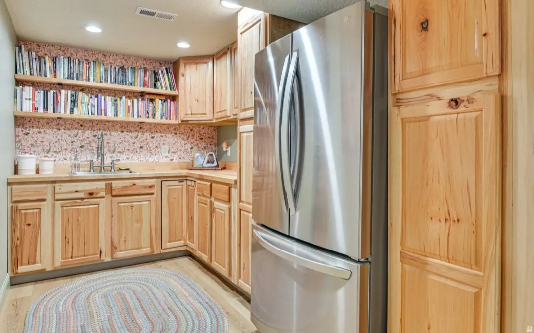 Recessed lighting illuminates wood-finish flooring and a built-in stainless steel refrigerator