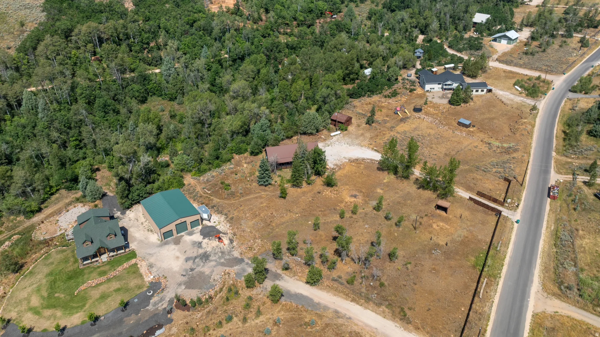 Expansive property featuring a residence with a covered porch, a large detached garage with two bay doors, and significant undeveloped land