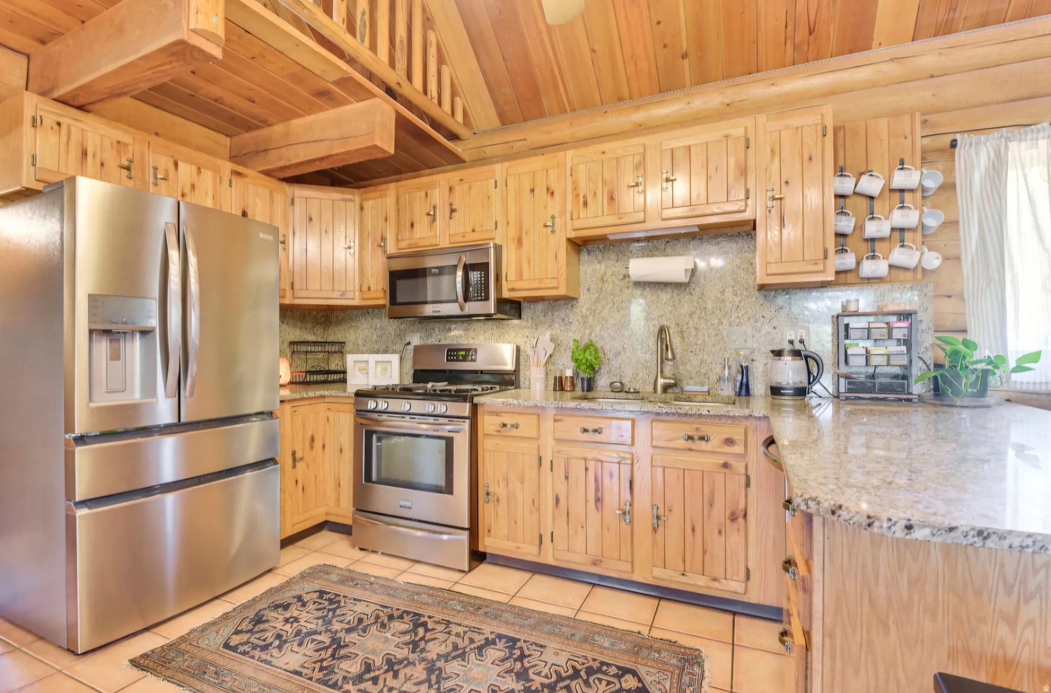 Kitchen featuring natural wood cabinetry, stainless steel appliances, granite countertops, and tile flooring