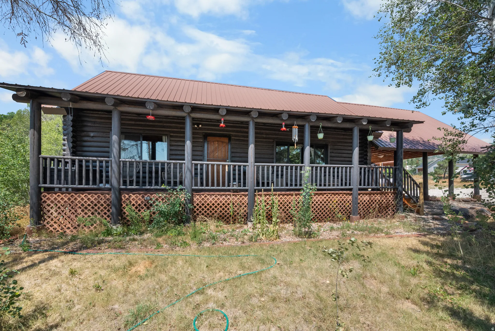 Log cabin exterior featuring a covered porch, dark wood log siding, and a reddish-brown metal roof