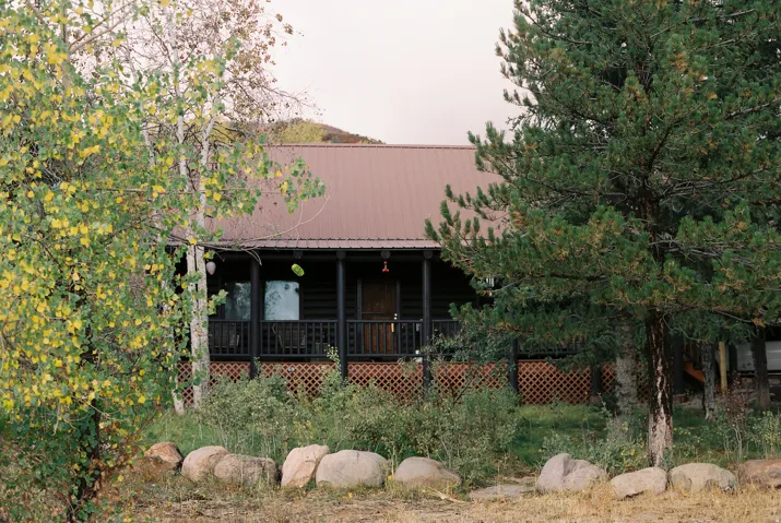 Log cabin exterior featuring a covered porch, dark brown metal roof, and exposed natural wood siding