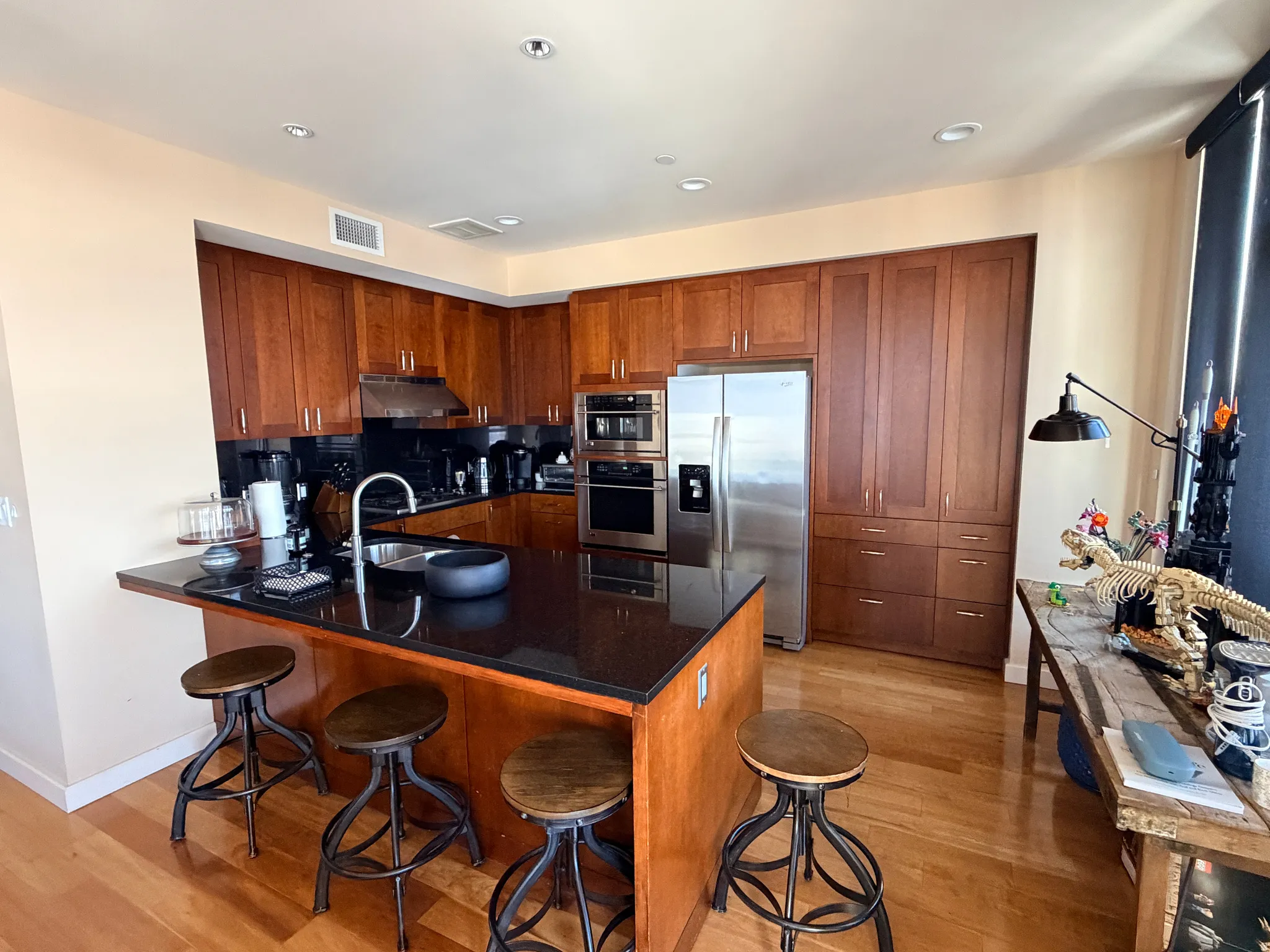 Full kitchen featuring rich wood cabinetry, stainless steel appliances, a black countertop island with integrated sink, recessed lighting, and wood-finish flooring