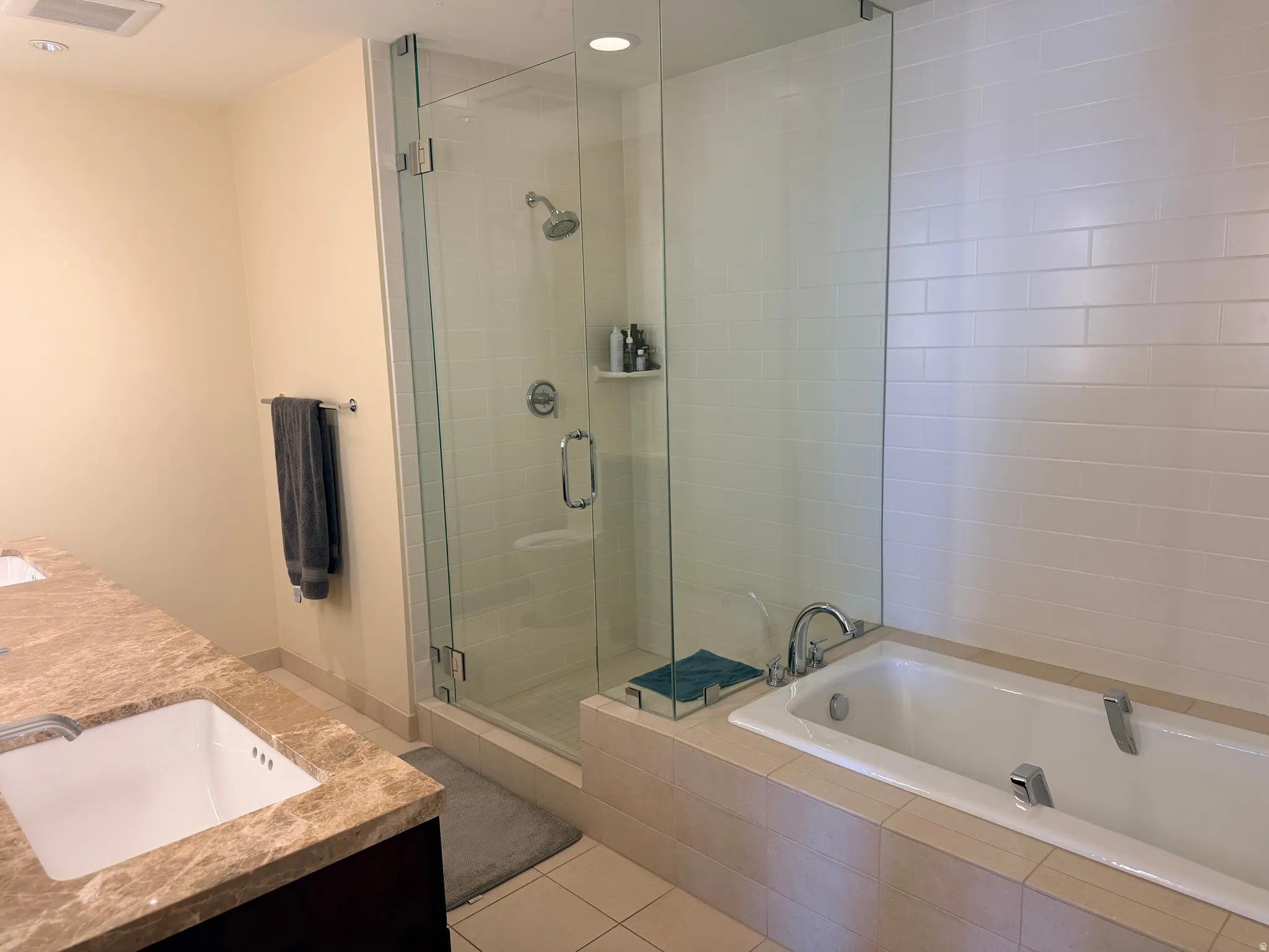 Bathroom featuring a glass-enclosed shower, a built-in soaking tub, and a dual-sink vanity with stone-finish countertops