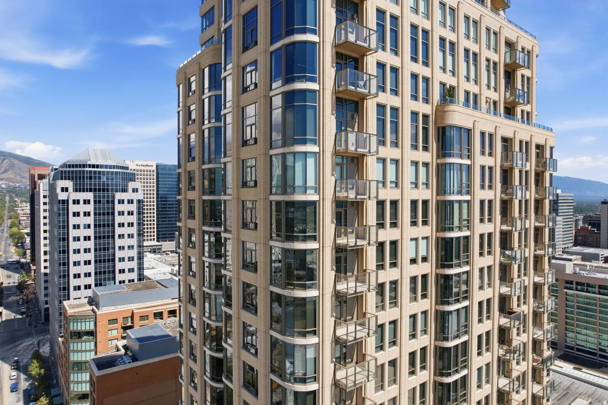 Contemporary mid-rise residential tower featuring curved glass balconies, warm-toned brick and stone façade, and abundant fenestration across multiple floors