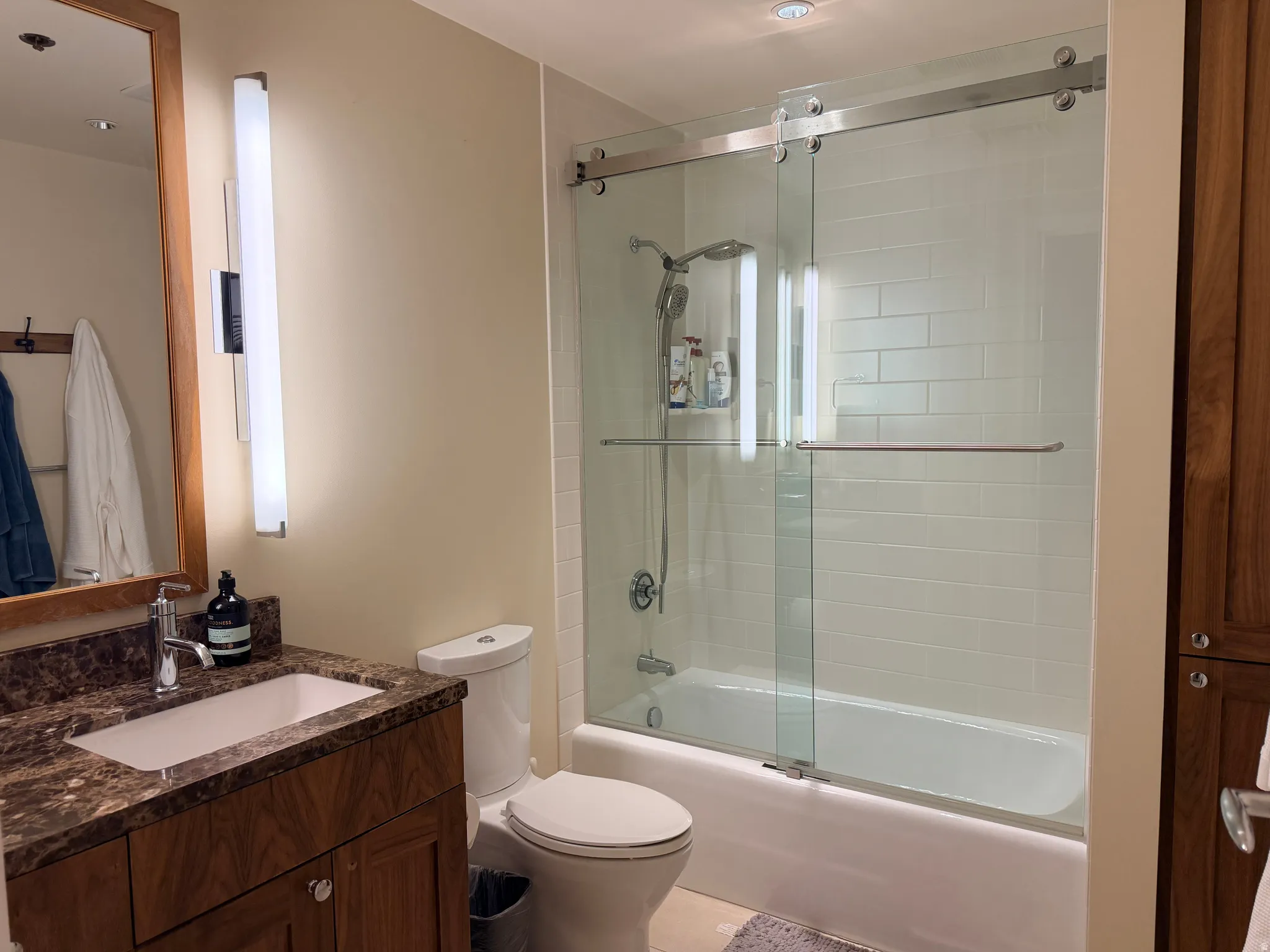 Modern bathroom featuring a wood-finish vanity with dual sinks and dark stone countertop, chrome fixtures, and recessed lighting