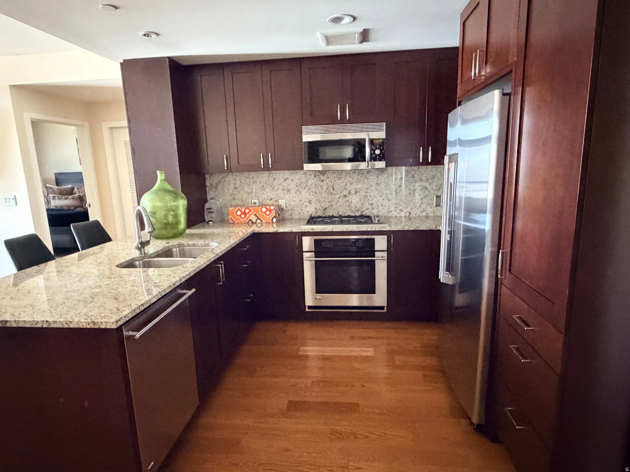 Kitchen featuring stainless steel appliances, wood-finish flooring, granite countertops, dark wood cabinetry, and a gas range