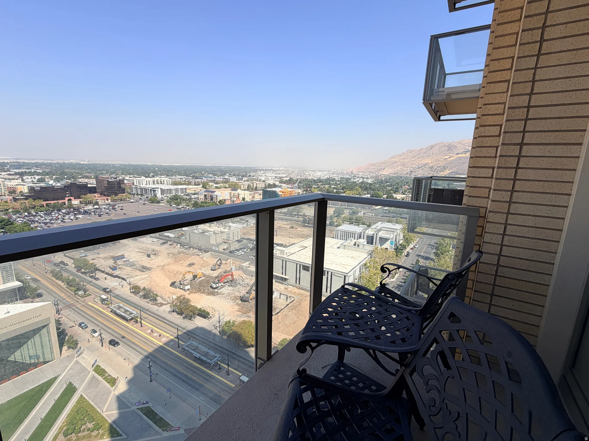 Balcony with glass railing overlooking the city, featuring a textured exterior wall and distant mountains