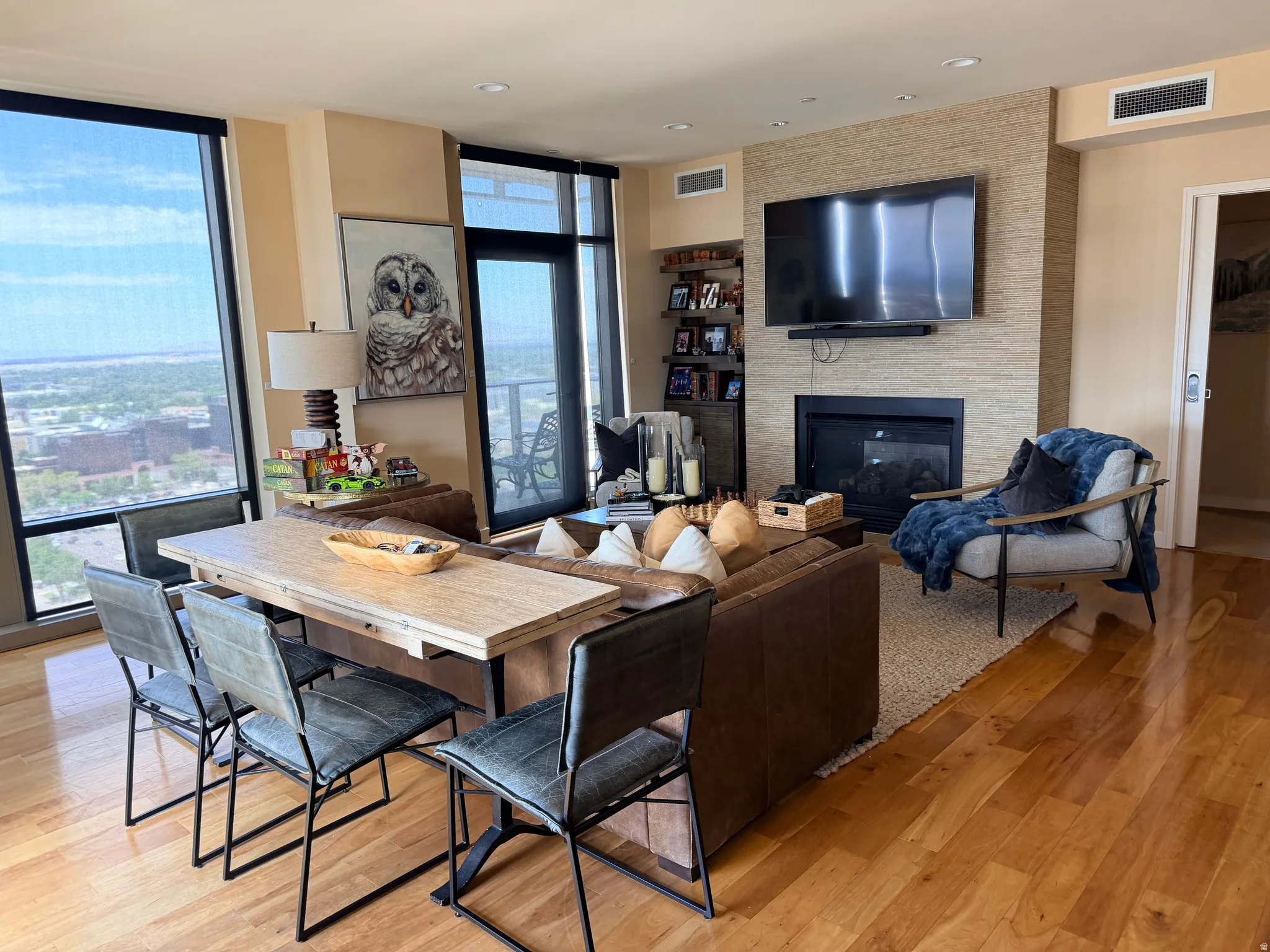Spacious living area featuring expansive windows with roller shades, a contemporary fireplace with a stone-finish surround, light wood-finish flooring, and recessed ceiling lighting