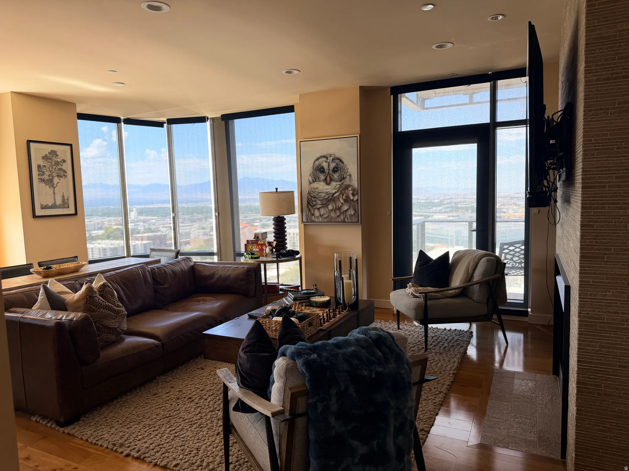 Expansive windows with roller shades frame city and mountain scenery