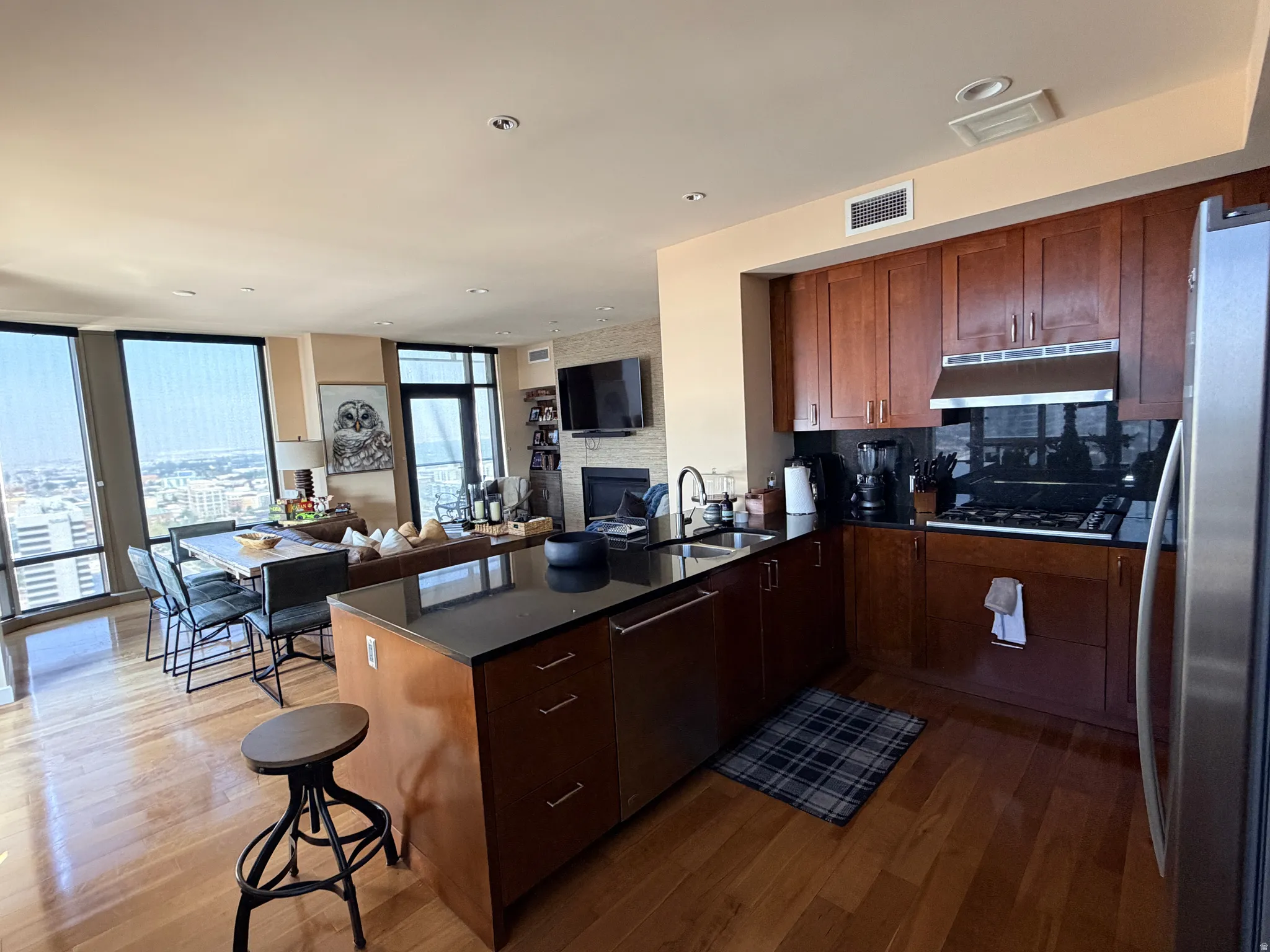 Open-concept kitchen featuring an island with a black countertop, rich wood cabinetry, stainless steel appliances, and a gas range