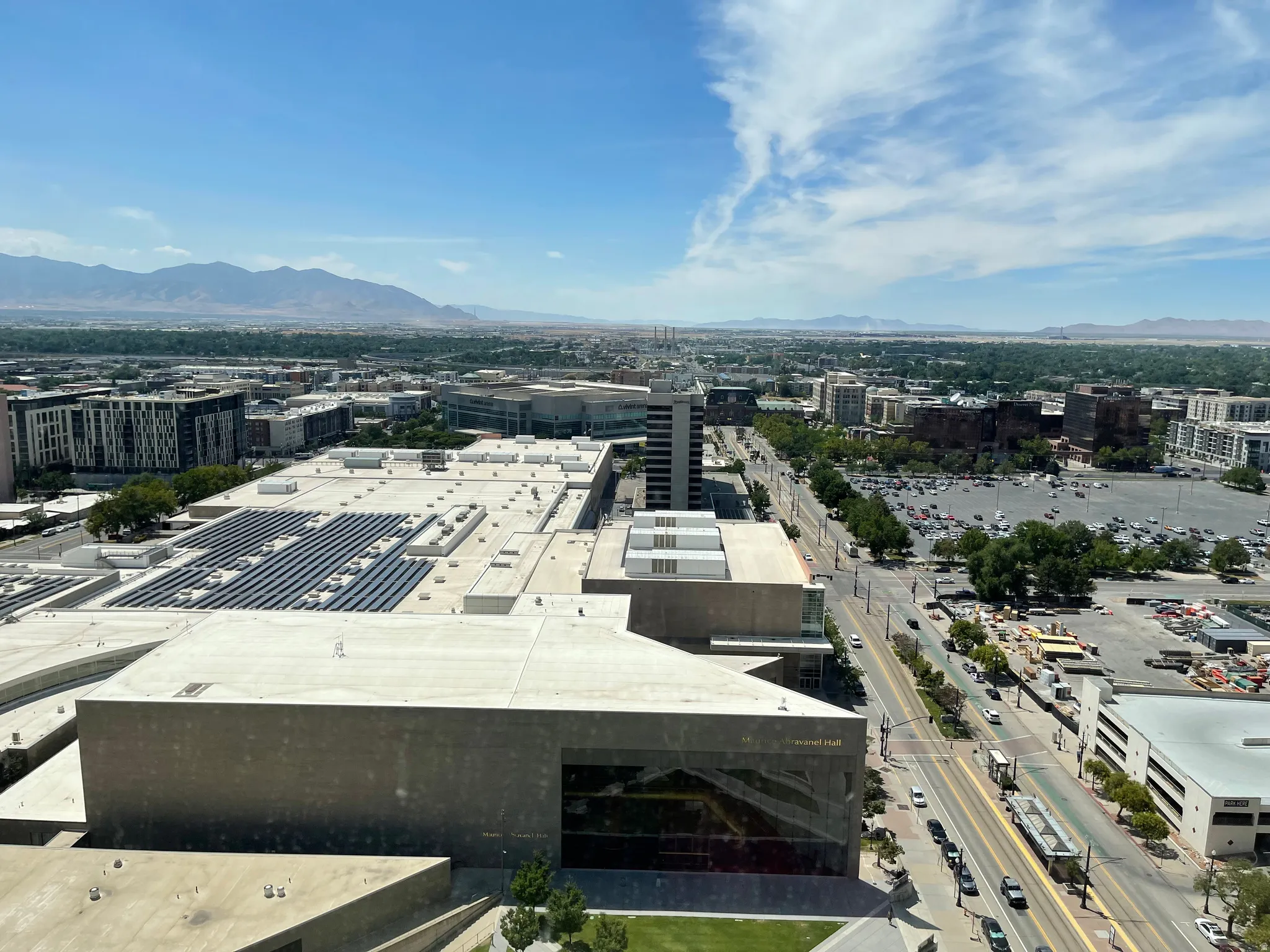Expansive cityscape vista featuring a prominent building with rooftop solar panels, a multi-lane thoroughfare, and distant mountains