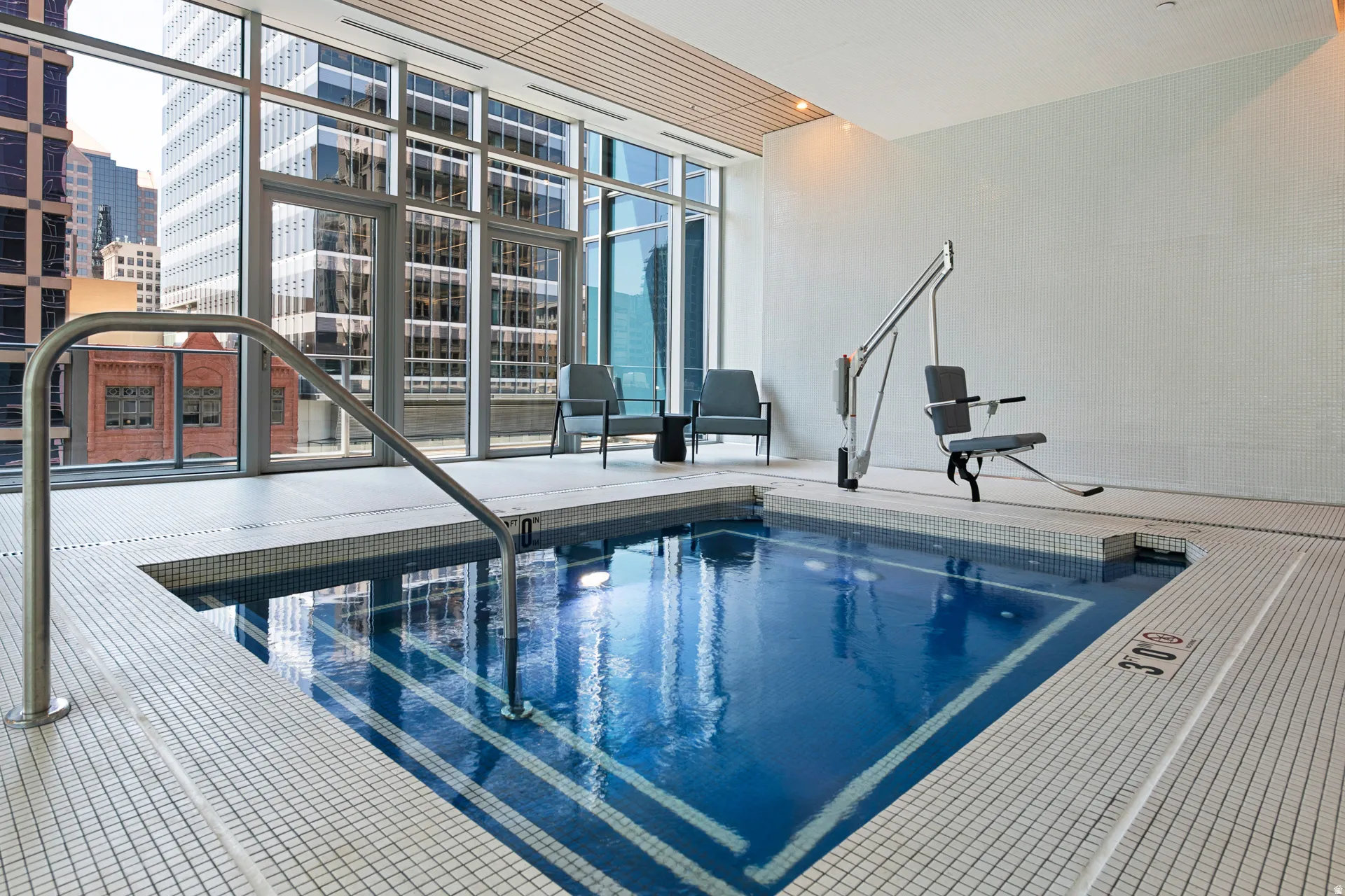 Indoor pool with a mosaic tile interior, stainless steel handrail, and an accessible lift