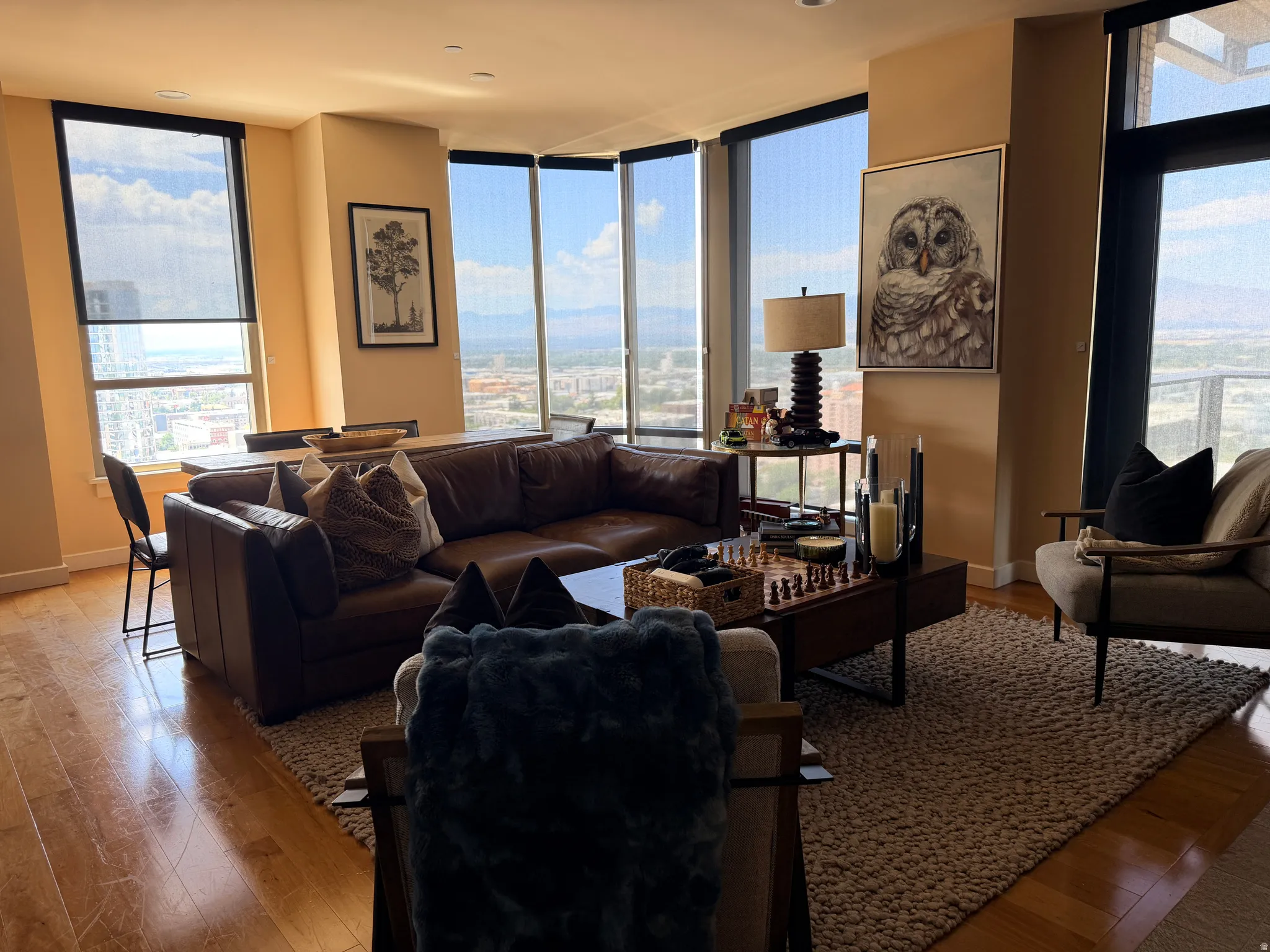Expansive living area featuring light wood-finish flooring, floor-to-ceiling windows with roller shades, and a corner dining space