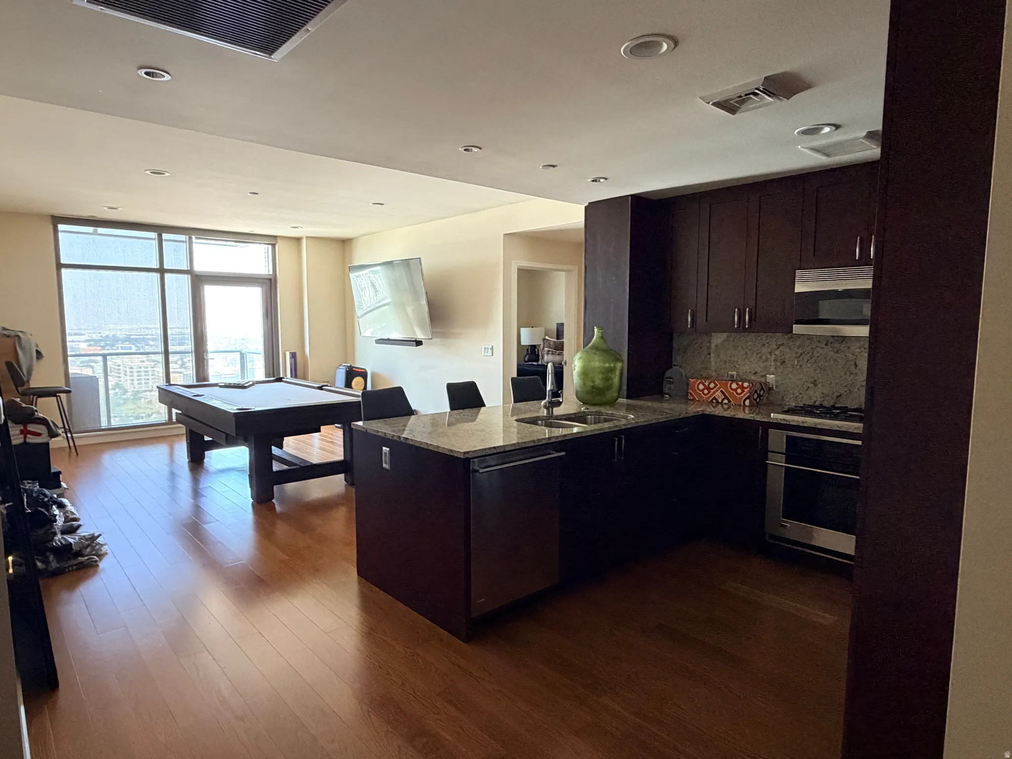 Open-concept living space featuring wood-finish flooring, a contemporary kitchen with dark wood cabinetry and stone countertops, and stainless steel appliances