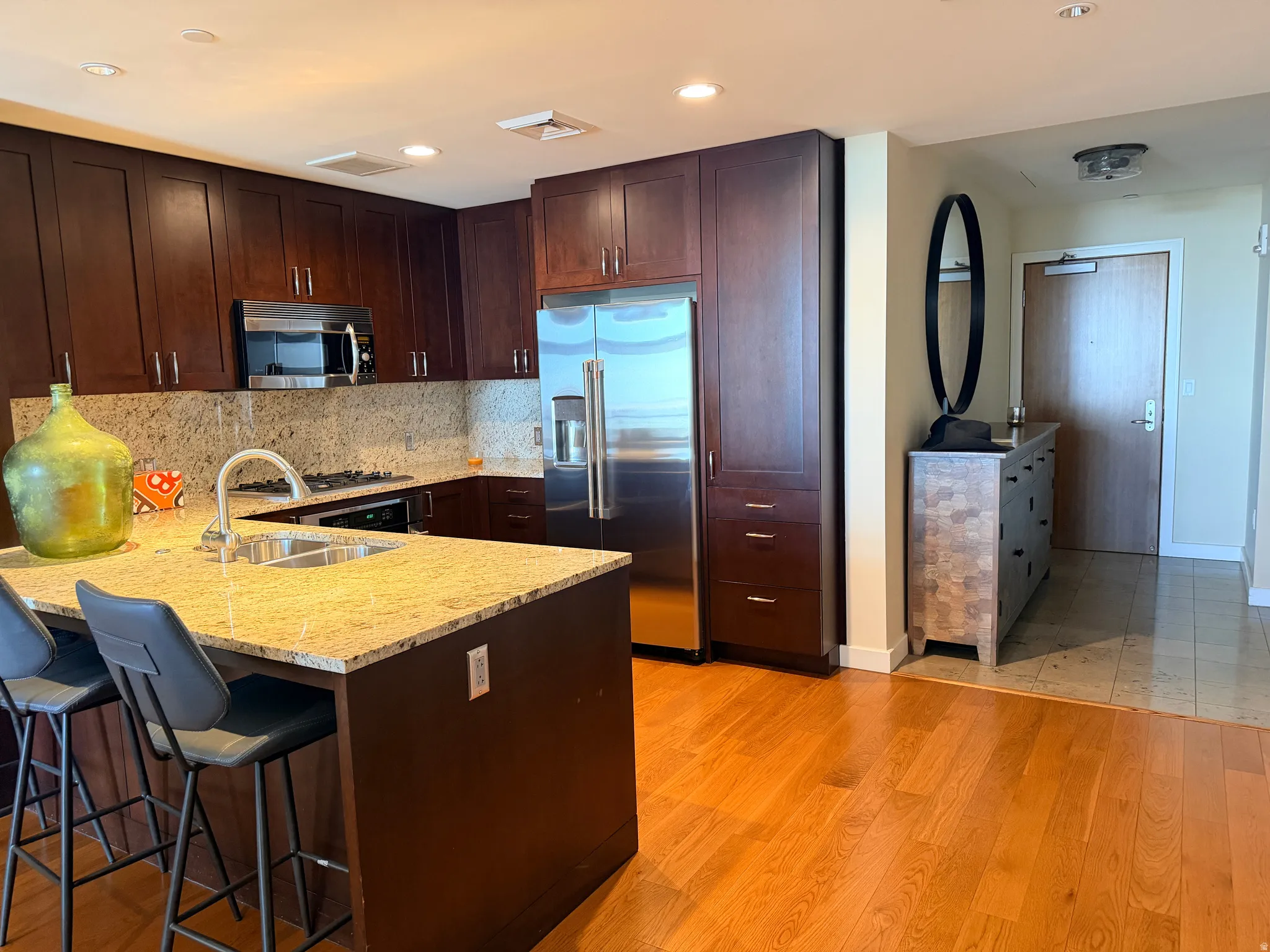 Gourmet kitchen featuring granite countertops, full-height backsplash, rich wood cabinetry, and stainless steel appliances