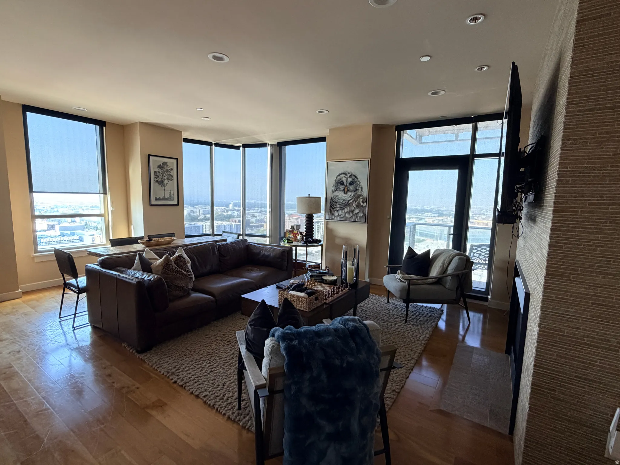 Expansive living space featuring hardwood flooring, recessed lighting, floor-to-ceiling windows with roller shades, and a built-in fireplace