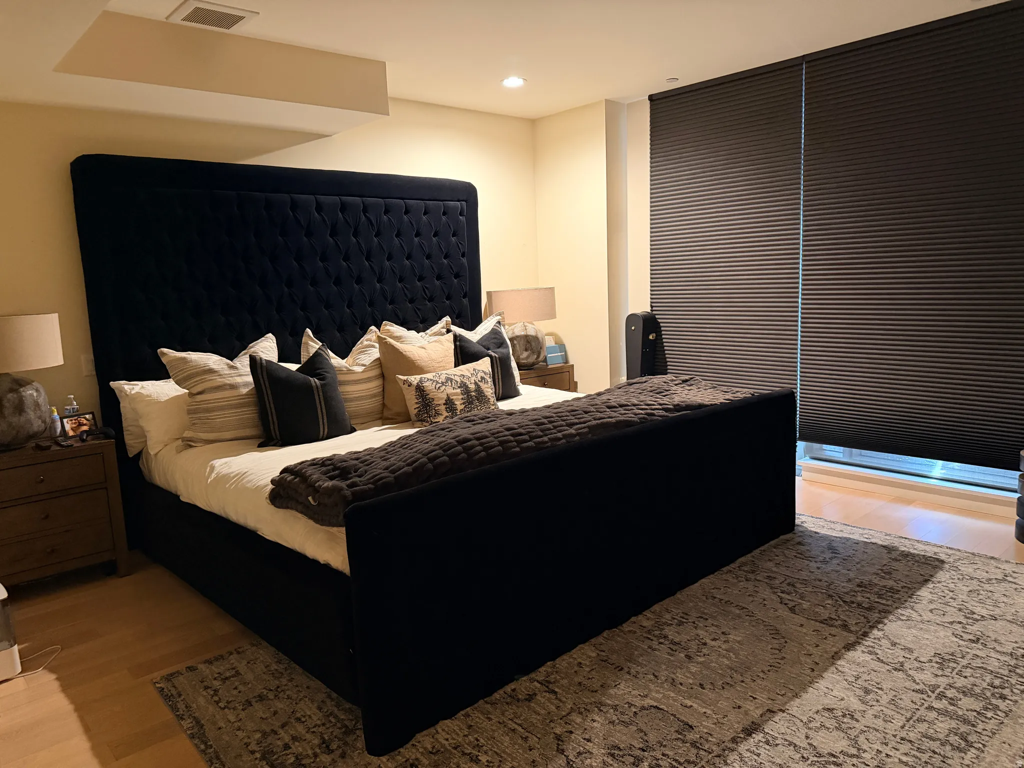Luxurious primary bedroom showcasing a striking black upholstered bed with diamond-quilted headboard, layered bedding in neutral tones, and coordinating throw pillows