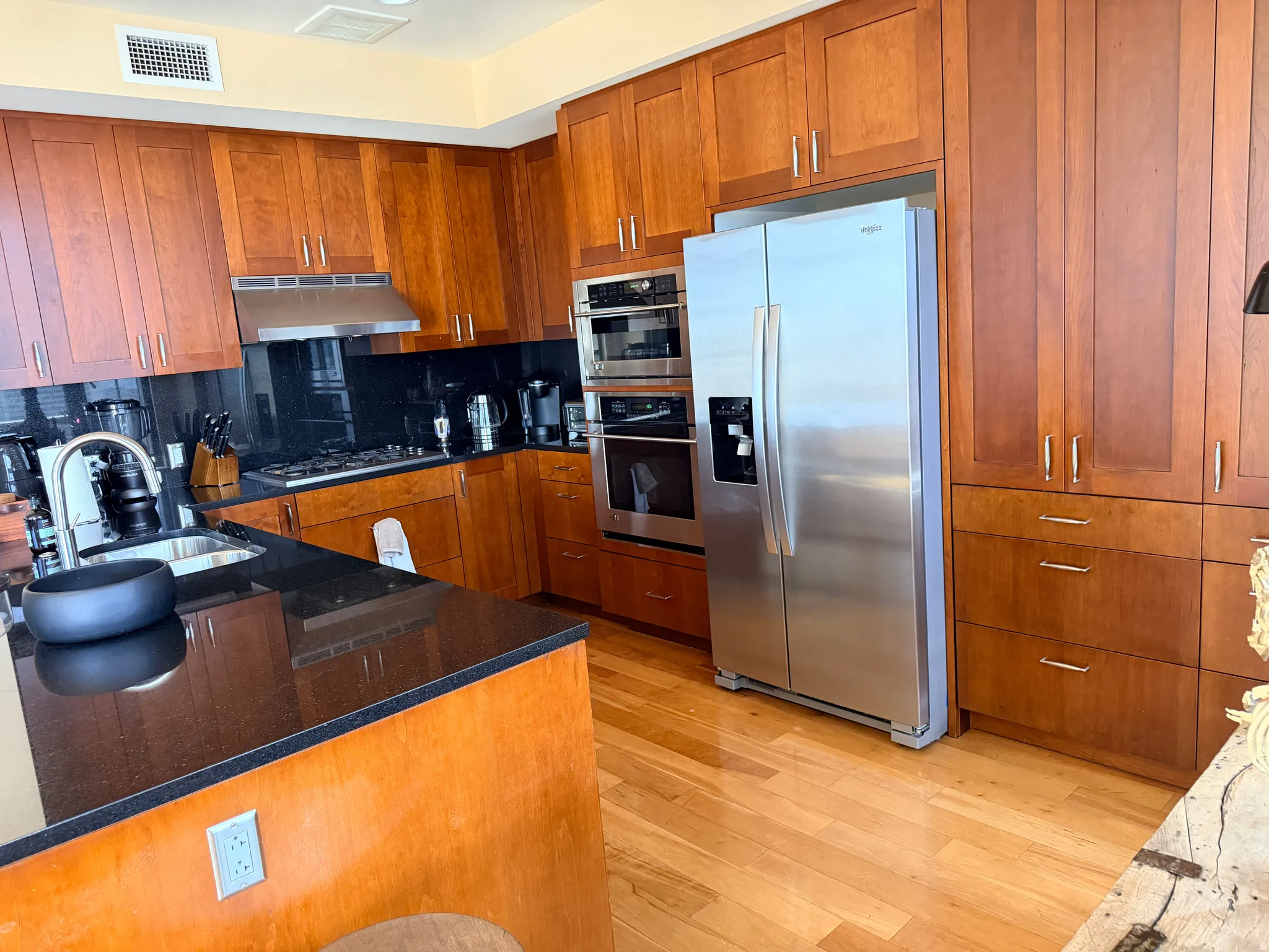 Warm wood cabinetry and stainless steel appliances define this chef's kitchen, featuring dual wall ovens, a spacious island with dark countertops, hardwood flooring, and abundant storage throughout