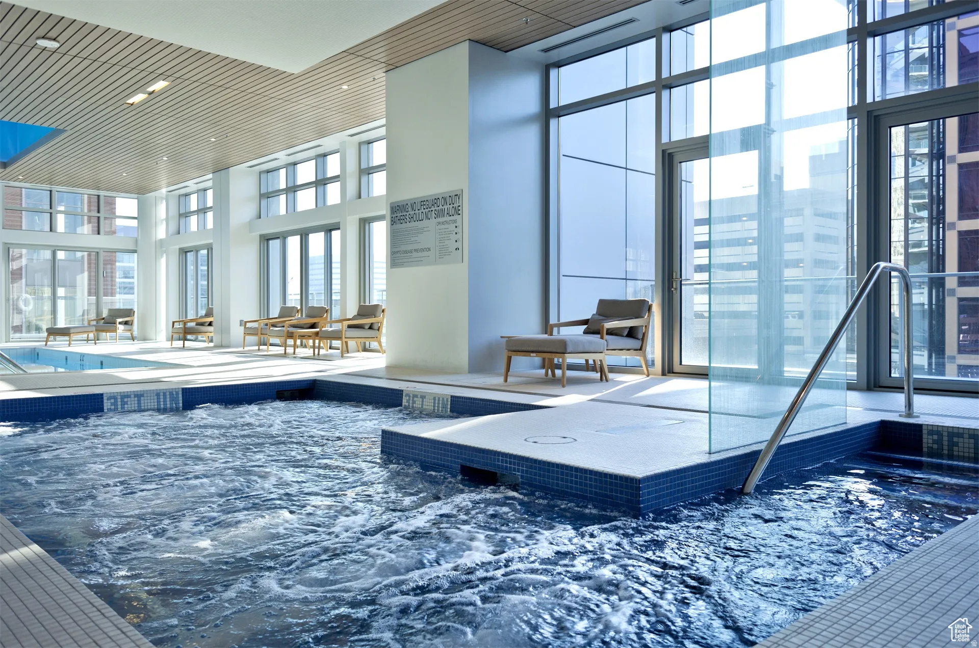 Indoor aquatic area featuring a bubbling spa, adjacent swimming pool, and extensive window walls
