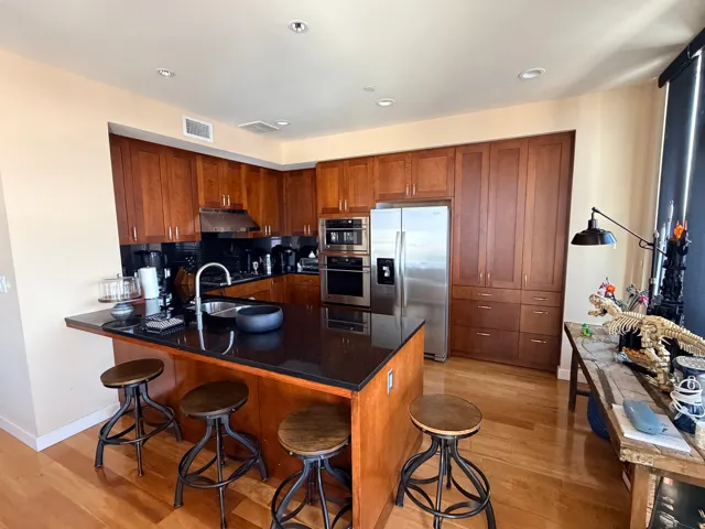 Full kitchen featuring rich wood cabinetry, stainless steel appliances, a black countertop island with integrated sink, recessed lighting, and wood-finish flooring