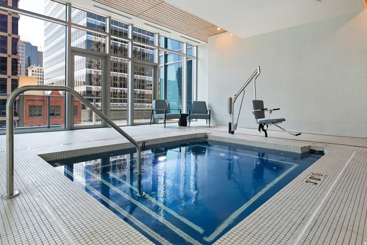 Indoor pool with a mosaic tile interior, stainless steel handrail, and an accessible lift