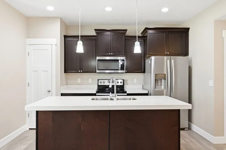Kitchen featuring dark wood-finish cabinetry, stainless steel appliances, a center island with an integrated sink, white countertops, and recessed lighting