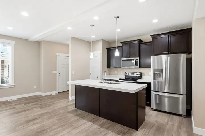 Open-concept kitchen featuring dark wood cabinetry, stainless steel appliances, and a central island with a white countertop