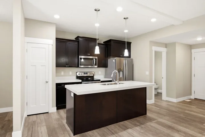 Modern kitchen featuring dark cabinetry with stainless steel appliances, white quartz countertops, and a substantial center island with pendant lighting