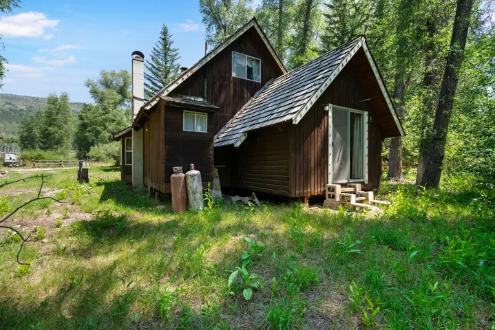 Wood-sided dwelling with a prominent A-frame section featuring a sliding glass door and an exterior chimney