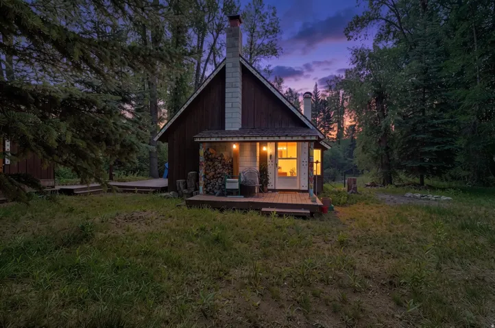Wood-sided cabin featuring a prominent stone chimney and a covered front porch