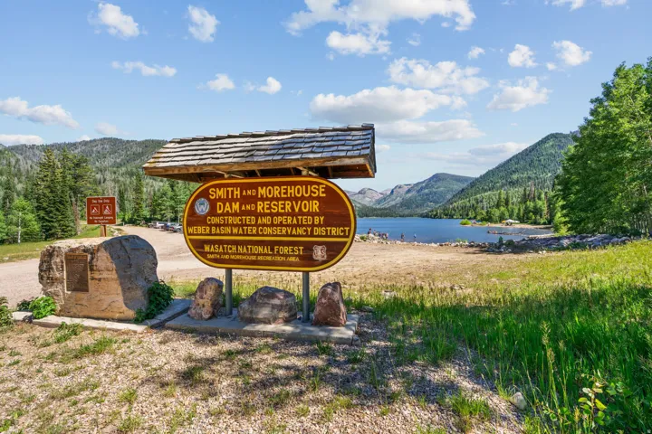 Reservoir entrance featuring a detailed informational sign with a shingled roof, a stone monument, and a gravel access road