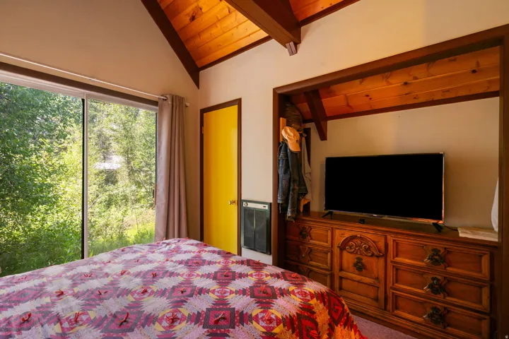 Vaulted wood-finish ceilings with exposed beams, large sliding glass doors, built-in media niche with wood-finish shelving, and a bright yellow door