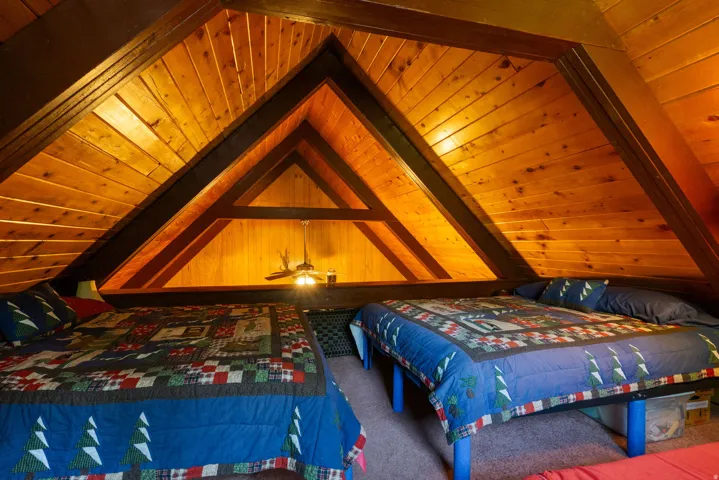 Attic space featuring pitched knotty pine walls and ceiling, exposed wooden beams, and a built-in light fixture