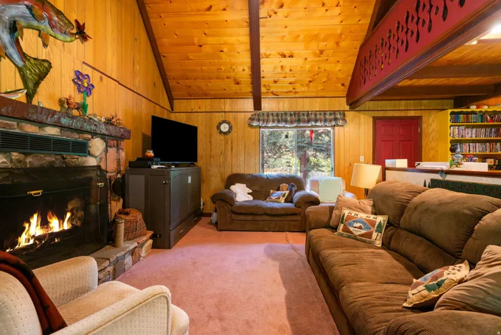Vaulted wood-paneled ceilings with exposed beams, a stone-surround fireplace, and a built-in entertainment center define this living space