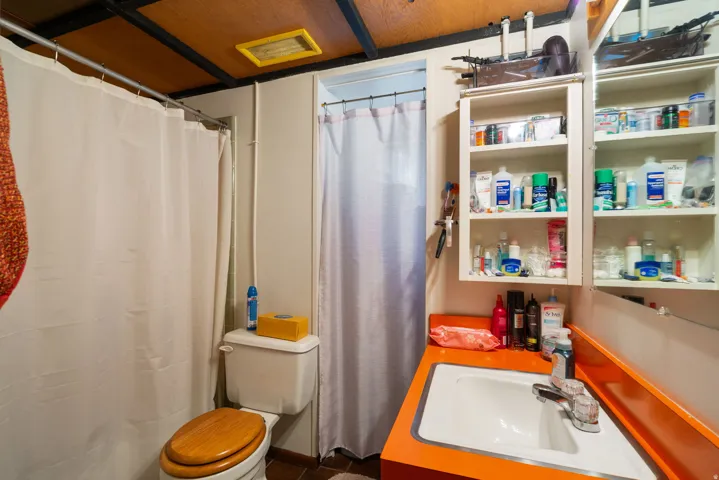 Bathroom featuring a white vanity sink with an orange countertop, built-in medicine cabinet with mirrored door, and wood-finish toilet seat