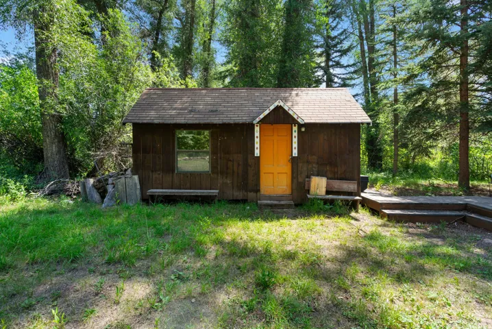 Wood-sided cabin featuring a contrasting orange entry door, single window, and a shingled roof