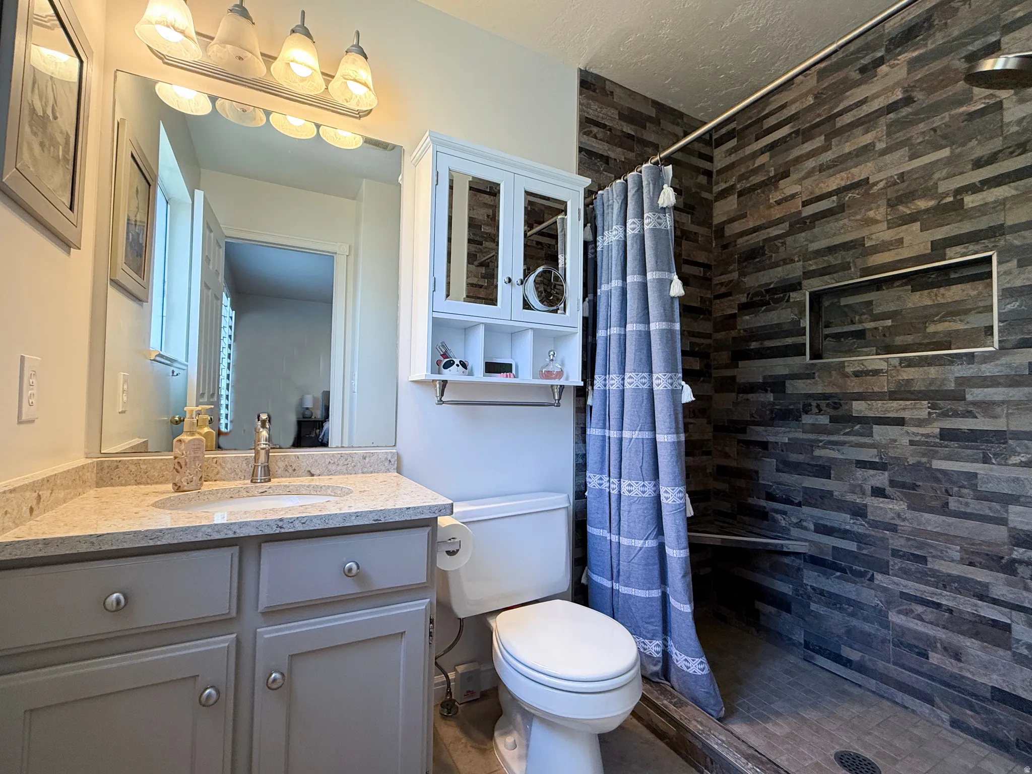 Bathroom featuring a vanity with an undermount sink and light-toned countertop, a wall-mounted cabinet, and a tiled shower enclosure