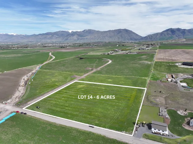 Six-acre lot featuring a green expanse, bordered by a paved road, with distant mountains