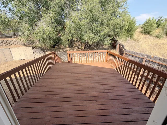 Spacious outdoor deck with wood railing, overlooking a fenced property perimeter