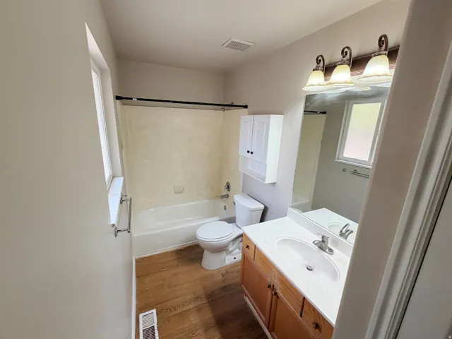 Full bathroom featuring a single window, a tub with shower, wood-finish flooring, a vanity with a single sink, and a wall-mounted medicine cabinet