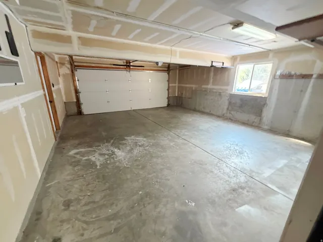 Attached garage with a concrete floor, overhead lighting, and a window