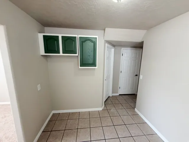 Tiled flooring, overhead cabinetry with dark green shaker-style doors, and light neutral wall paint