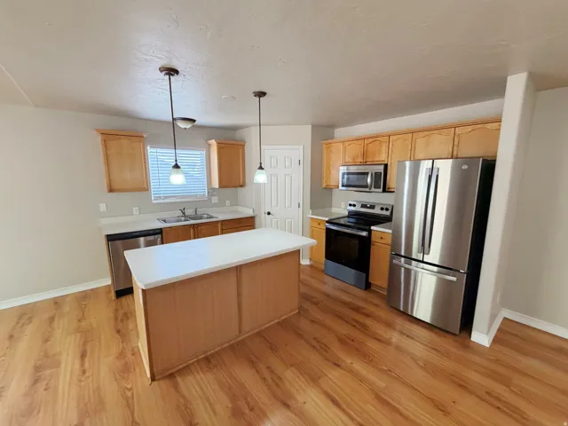Kitchen featuring wood-finish flooring, light wood cabinetry, stainless steel appliances, a center island with a white countertop, and pendant lighting
