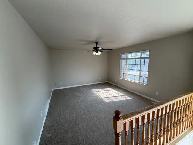 Spacious room featuring neutral carpeting, a large window with blinds, a ceiling fan, and painted walls